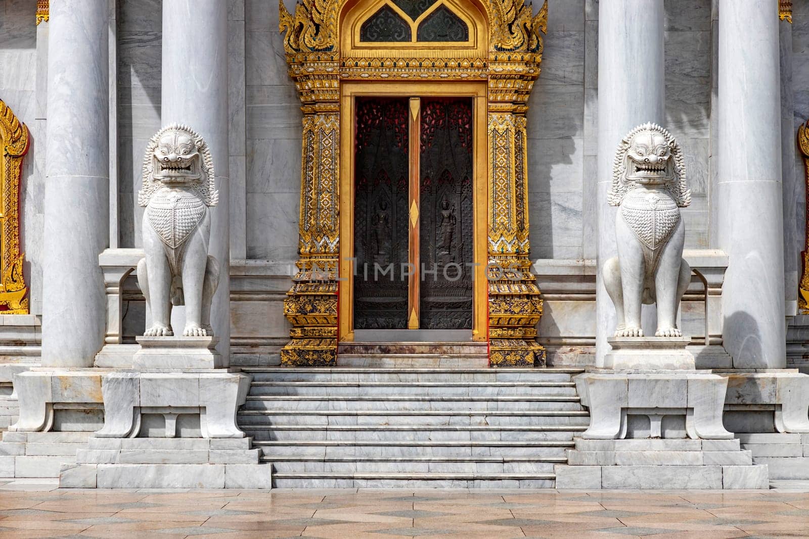 Pair of marble lions in front of the door of Wat Benchamabophit Dusit Wanaram (This temple is known as the Marble Temple) in Bangkok, blue sky and clouds. One of the most beautiful Thailand temples