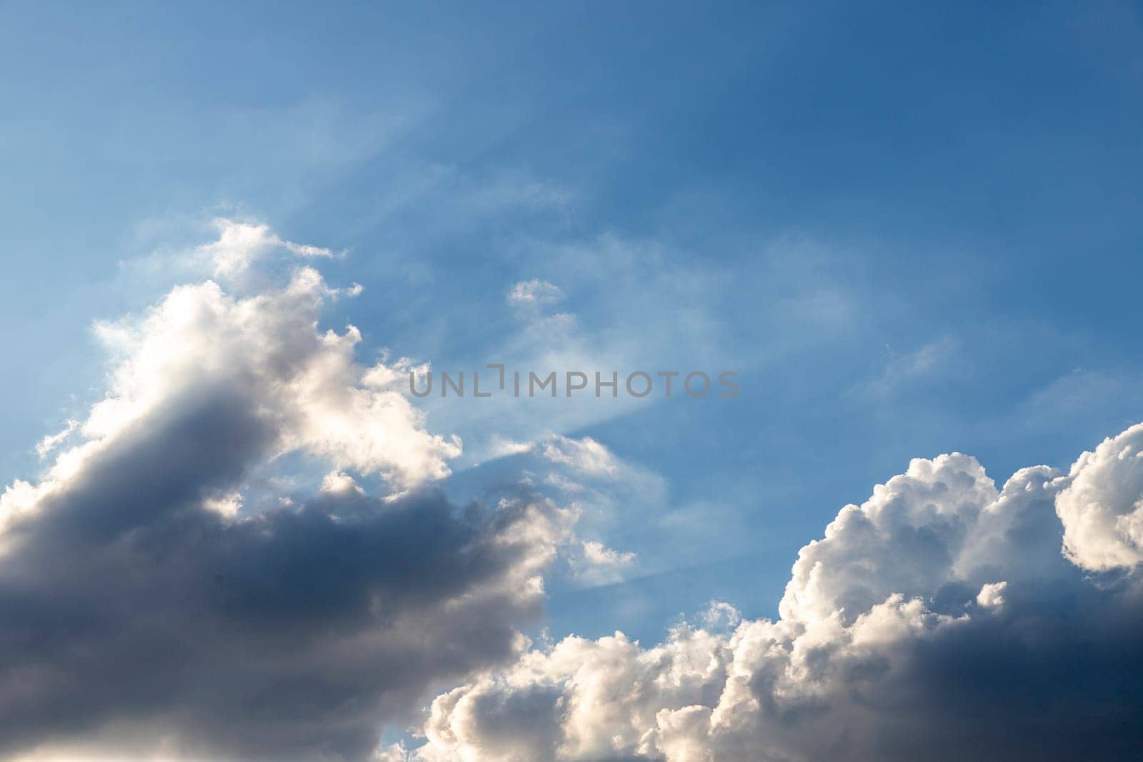 The blue sky has dark clouds at the bottom of the picture. and the sunlight shines from the bottom left corner of the picture