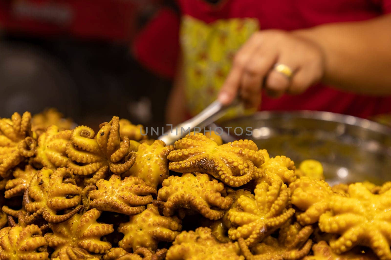 Whole octopus, small size, grilled with sauce until golden. Appetizing. Big piles and Chef stands blurry in the background. Selective focus.