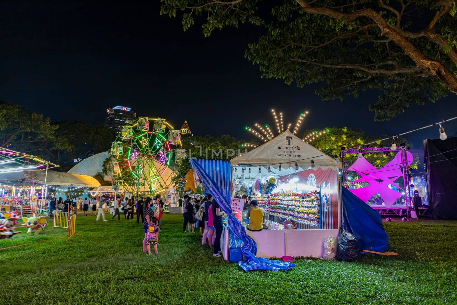 Bangkok, Thailand - Dec 8, 2022 : Crowds of people walk into a beautifully lit amusement park during the Red Cross Fair to be held from December 8-18, 2022. The image is blurred by the movement.