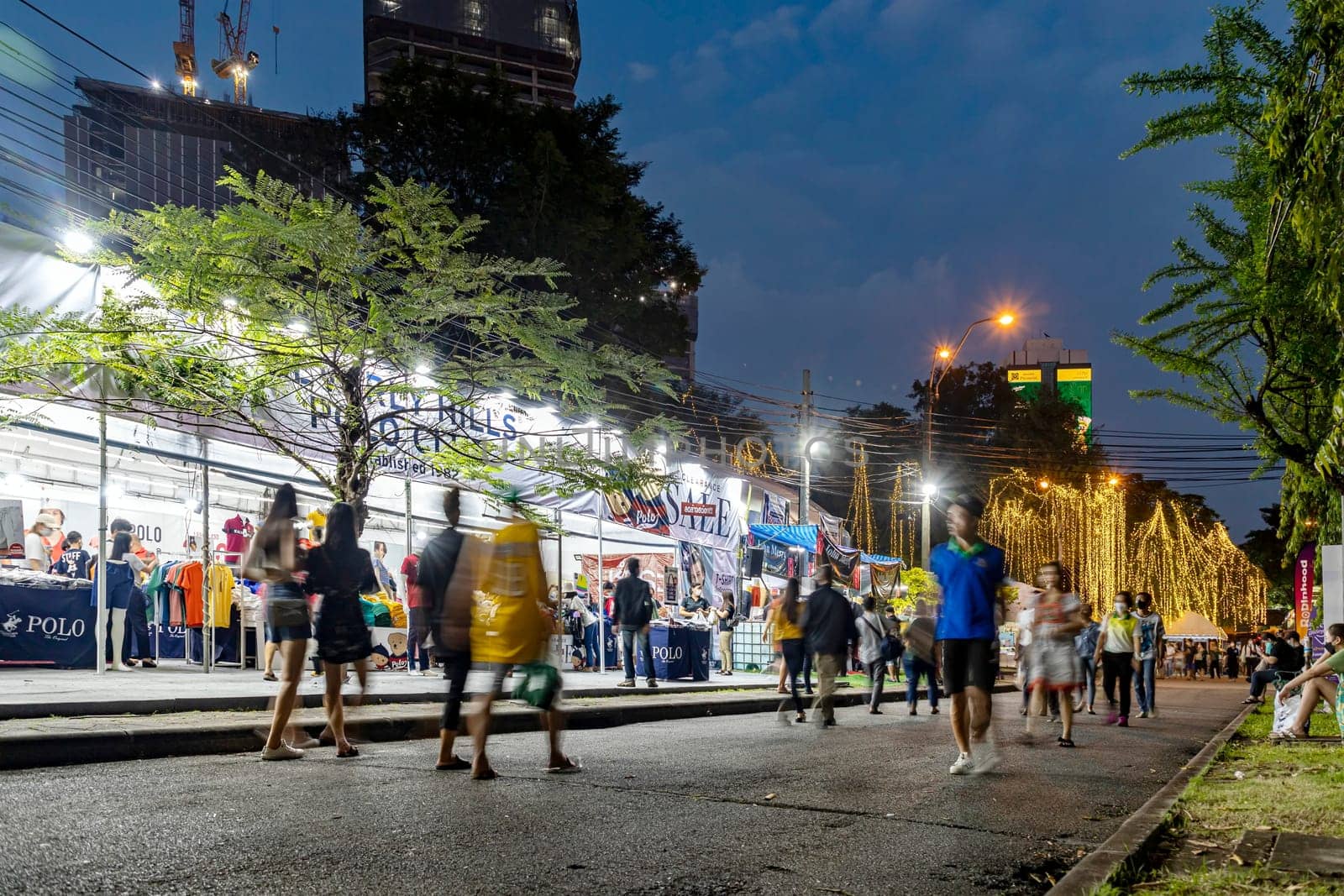 Bangkok, Thailand - Dec 8, 2022: Many people come for a walk at the Red Cross fair in Lumpini Park from December 8-18, 2022 at night. Some people sit and rest. There are many shops. Motion blur.