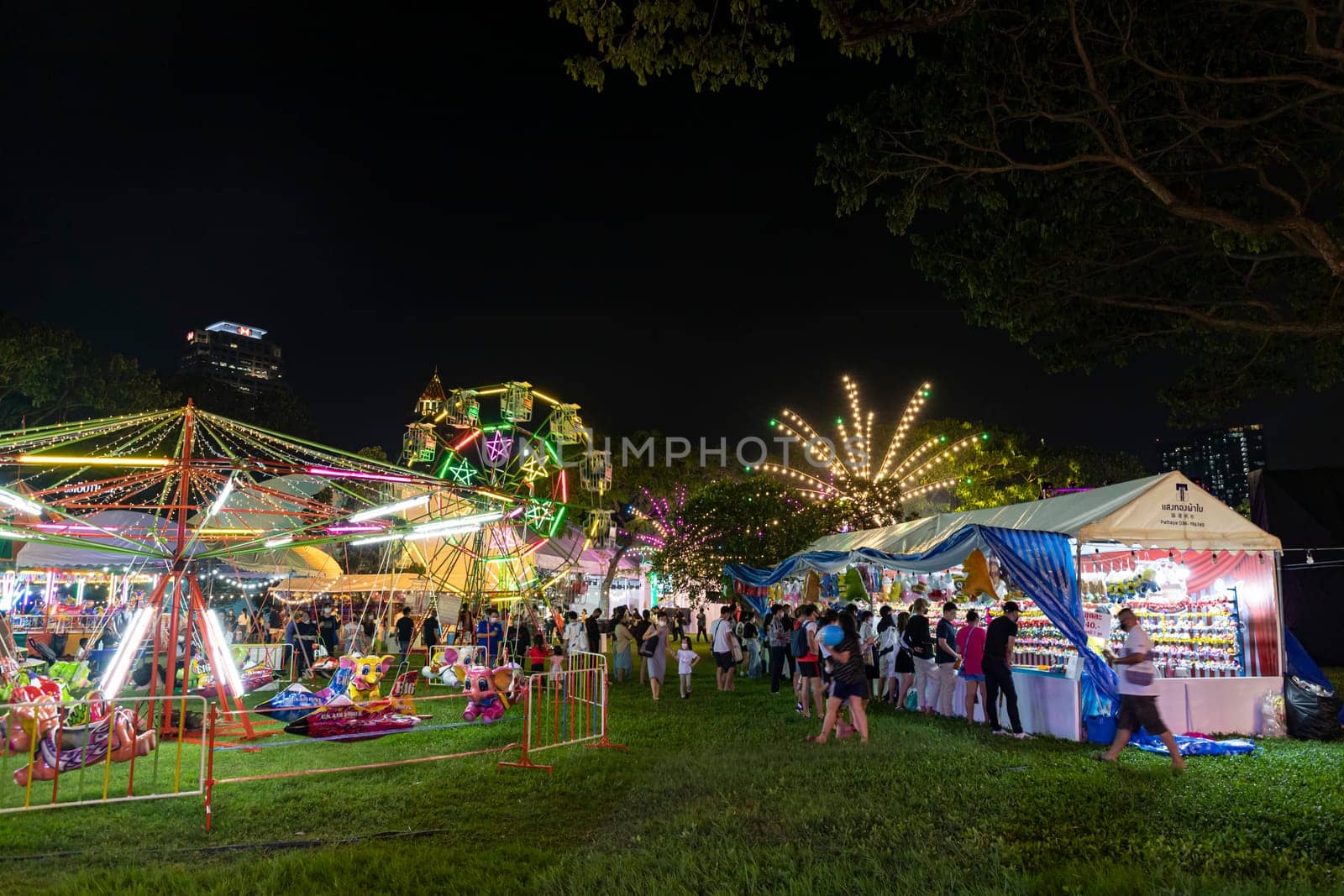 Bangkok, Thailand - Dec 8, 2022 : Crowds of people walk into a beautifully lit amusement park during the Red Cross Fair to be held from December 8-18, 2022. The image is blurred by the movement.