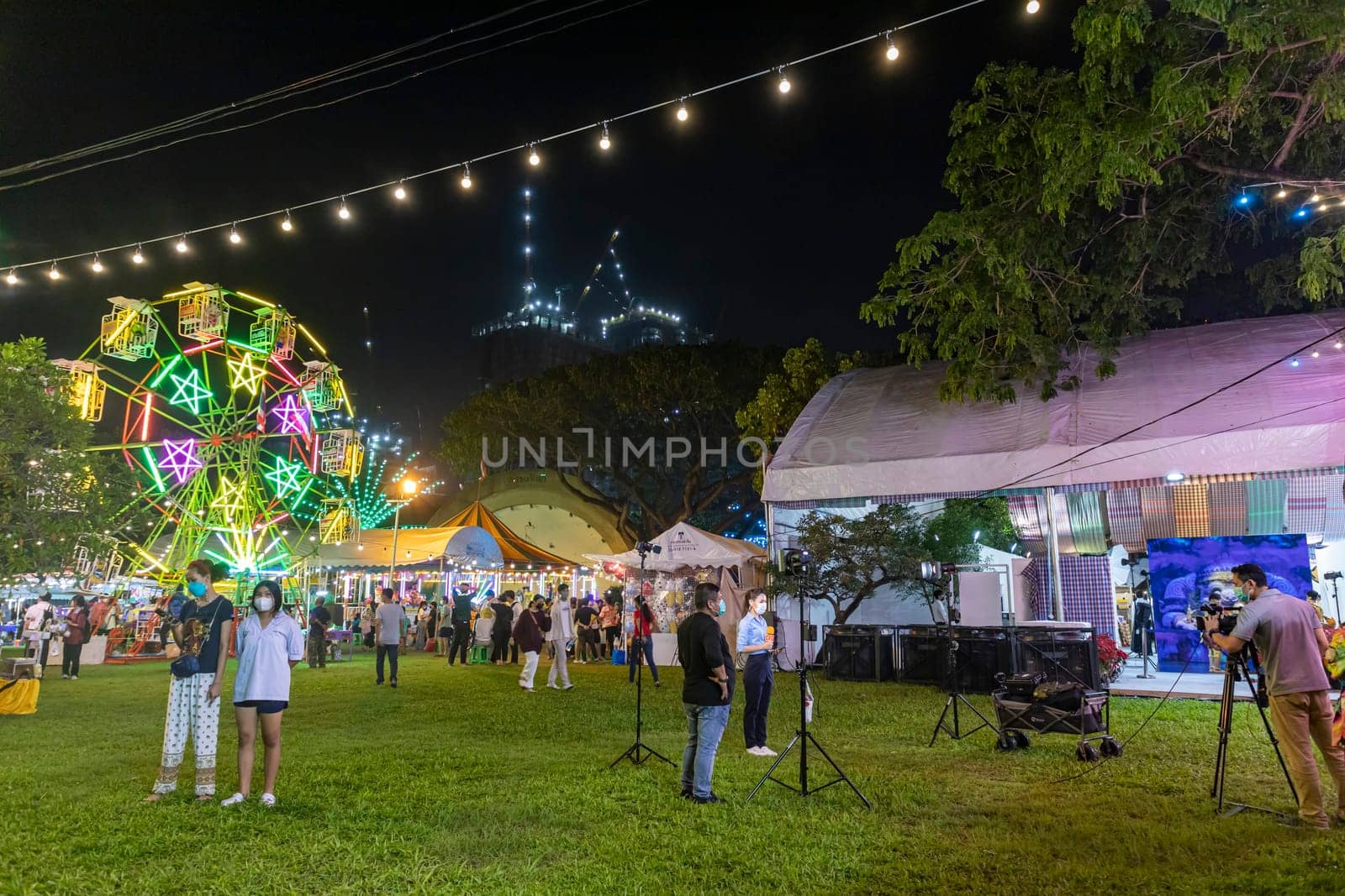 Bangkok,Thailand - Dec 8, 2022: A local reporter is reporting with a Ferris wheel in the background. during the Red Cross Fair to be held from December 8-18, 2022. The image is blurred by the movement