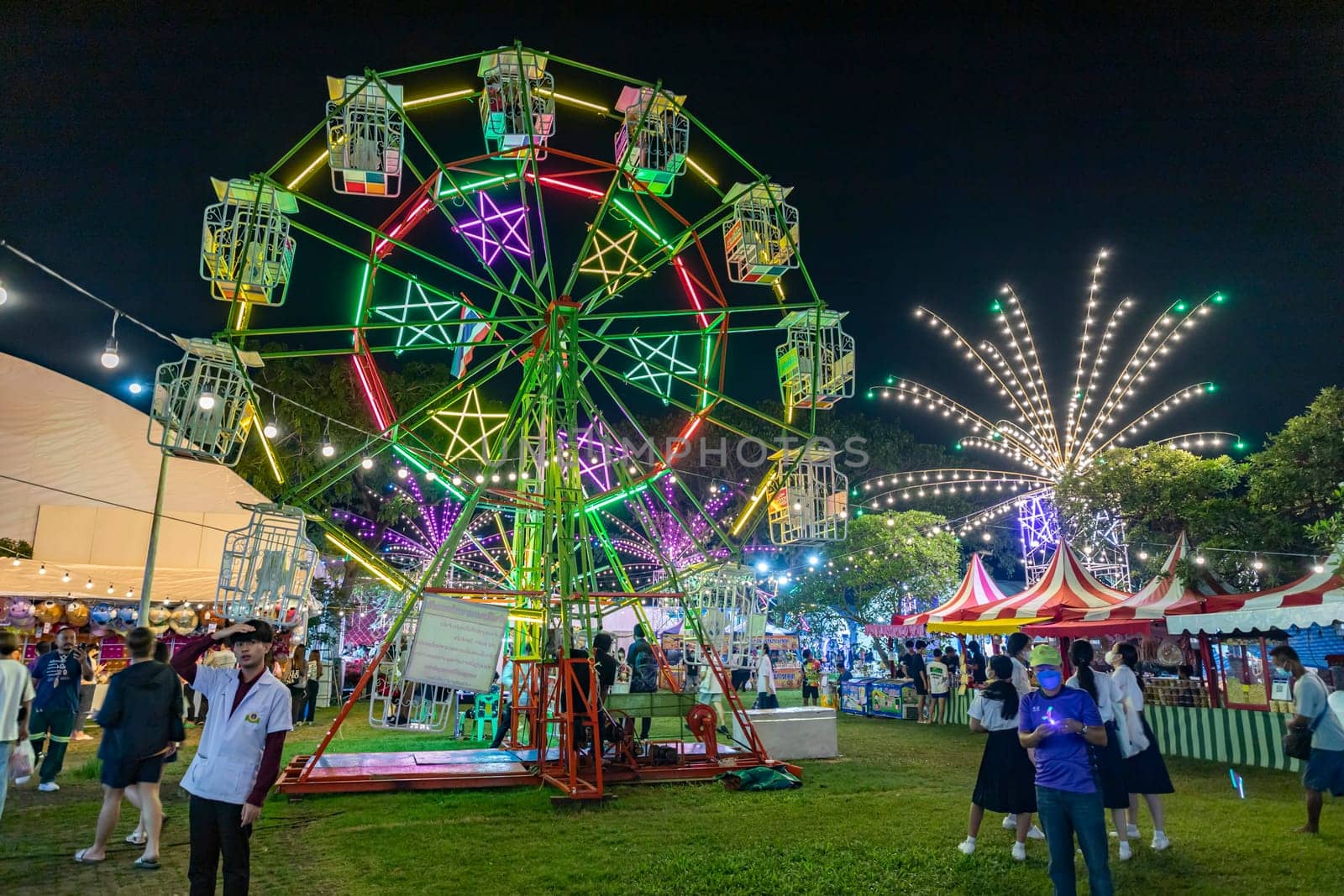 Bangkok, Thailand - Dec 8, 2022 : Crowds of people walk into a beautifully lit amusement park during the Red Cross Fair to be held from December 8-18, 2022. The image is blurred by the movement.