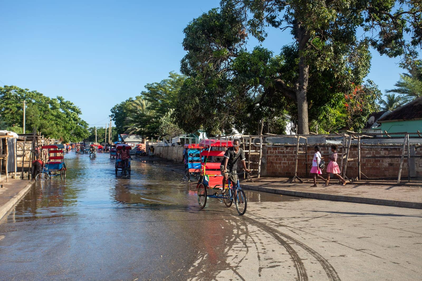 Toliara, Madagascar - November 21. 2022: Traditional rickshaw bicycle with Malagasy passengers on the street, one of the ways to earn money. Everyday life on the cities street of Madagascar.