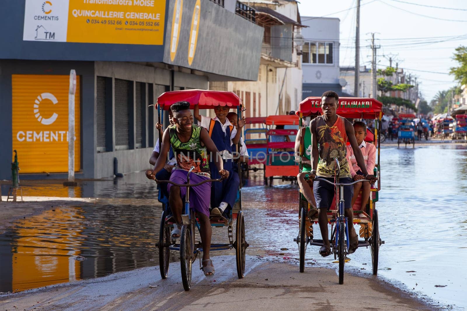 Toliara, Madagascar - November 21. 2022: Traditional rickshaw bicycle with Malagasy passengers on the street, one of the ways to earn money. Everyday life on the cities street of Madagascar.