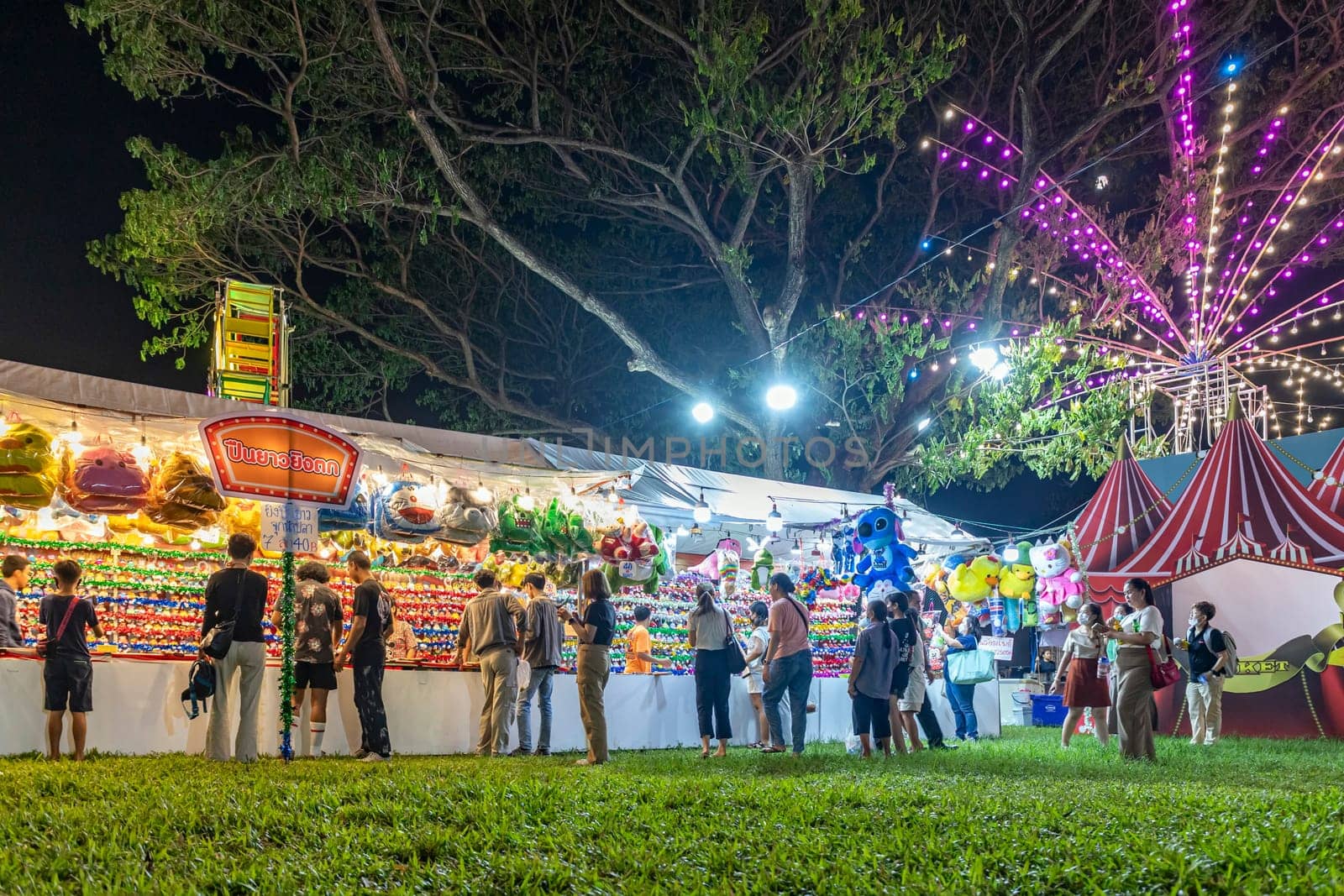 Bangkok, Thailand - Dec 8, 2022: Visitors to the Red Cross Fair at Lumpini Park, held from December 8-18, 2022, are shooting airsoft rifles to win colorful dolls. ฺBeautiful lights. Motion blur.