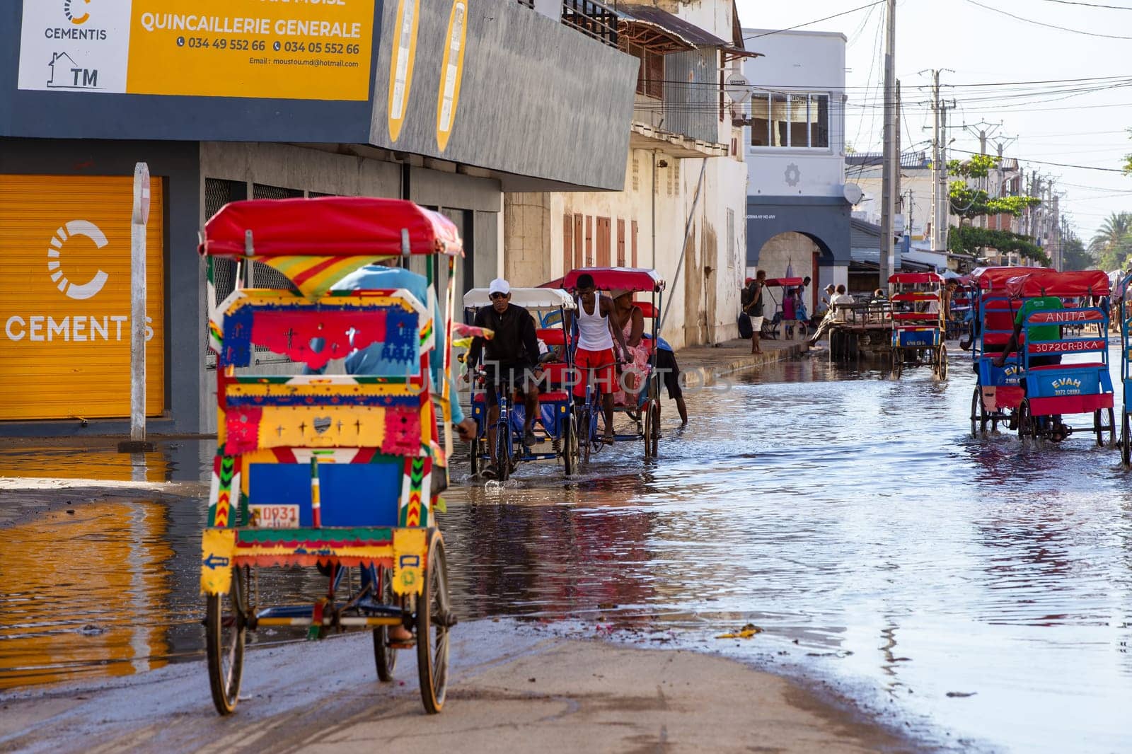 Toliara, Madagascar - November 21. 2022: Traditional rickshaw bicycle with Malagasy passengers on the street, one of the ways to earn money. Everyday life on the cities street of Madagascar.