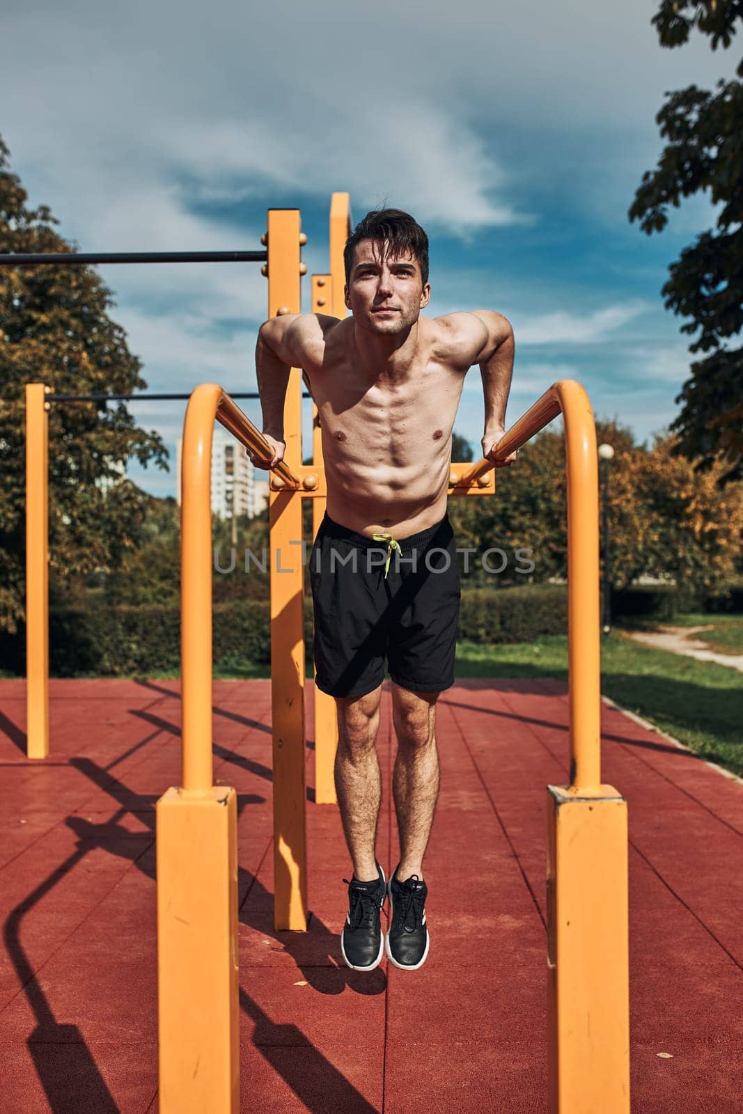 Young shirtless bodybuilder doing dips on parallel bars during his workout in a modern calisthenics street workout park
