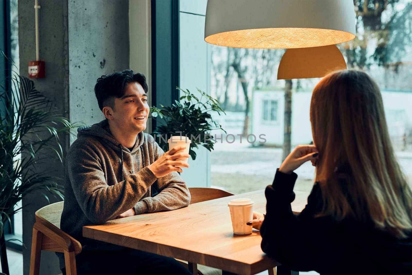 Friends having a chat, talking together, drinking coffee, sitting in a cafe. Young man and woman having a break, relaxing in cafe