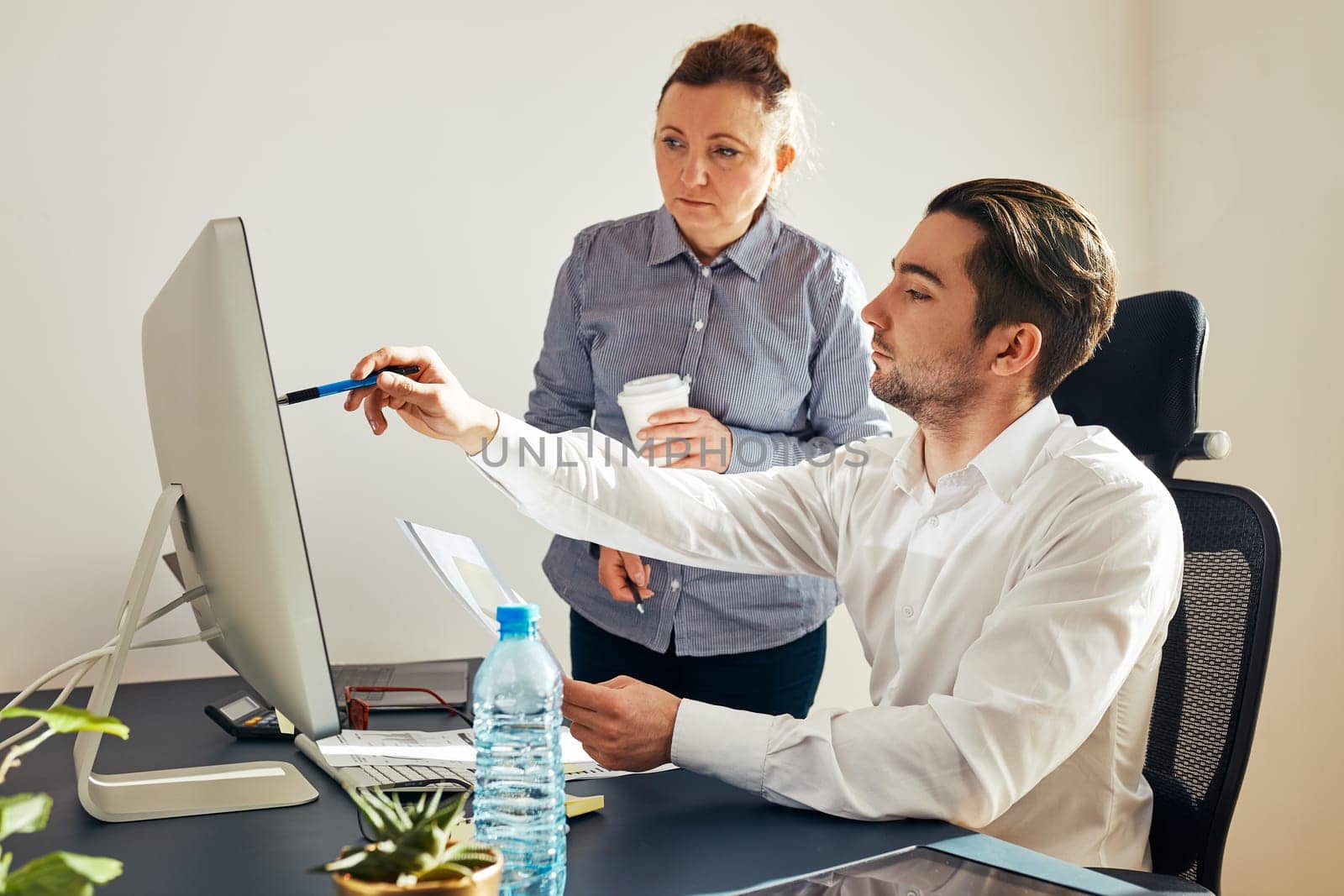 Two business people discussing financial data on computer. Businesswoman working with male colleague in office. People entrepreneurs working with charts and tables on screen. Two people working together. Workmates talking about project