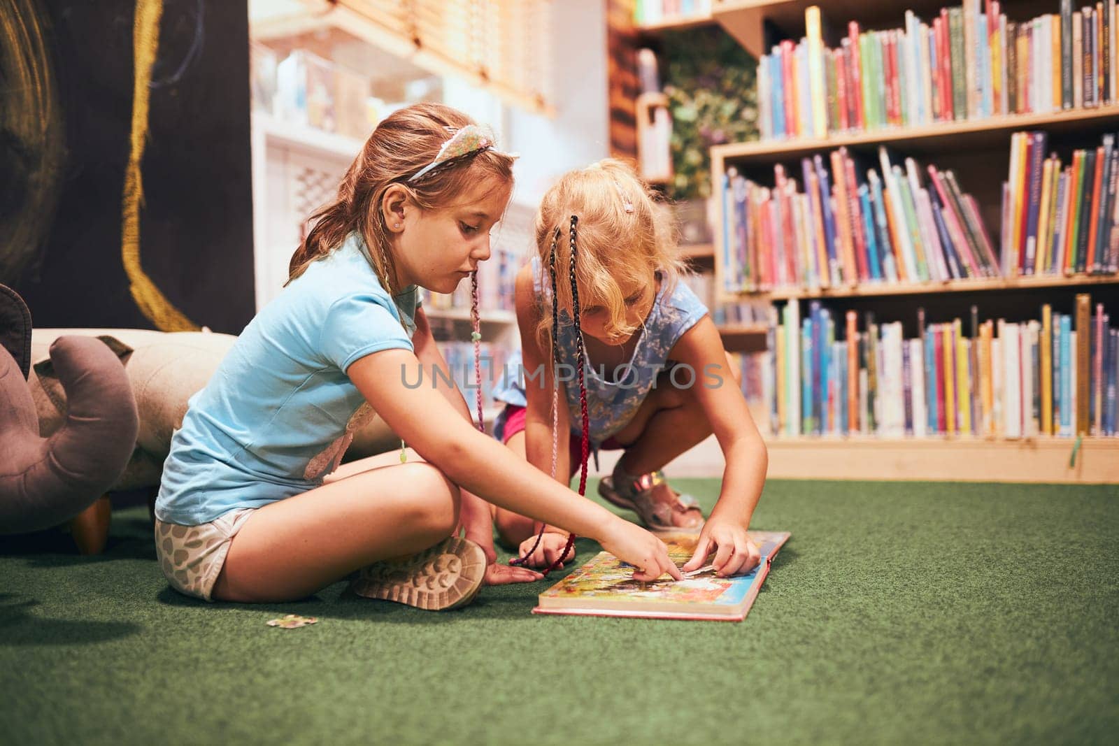 Two elementary schoolgirls solving puzzles and riddles in school library. Students learning from books. Pupils having fun in library. Back to school