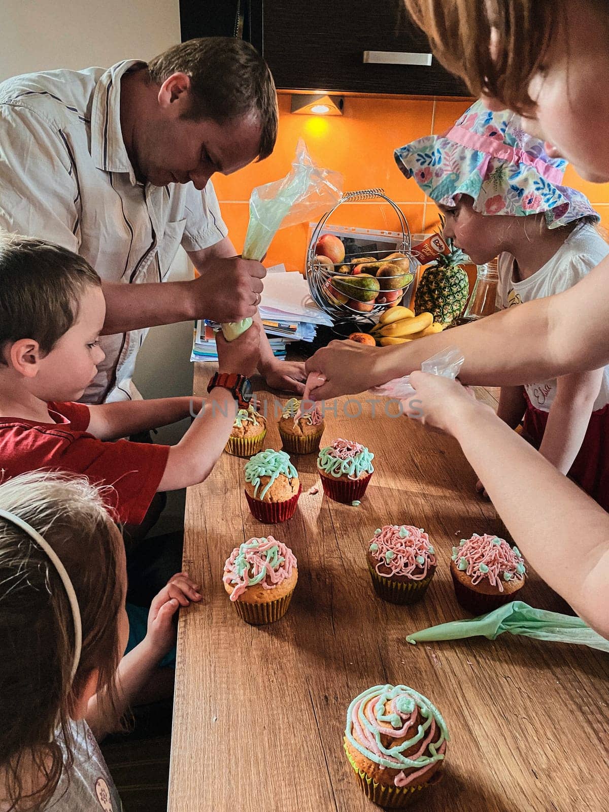 Group of children baking cupcakes, squeezing cream from confectionery bag, preparing ingredients, topping, sprinkles for decorating cookies. Kids cooking, working together in kitchen at home. Concept of happy family