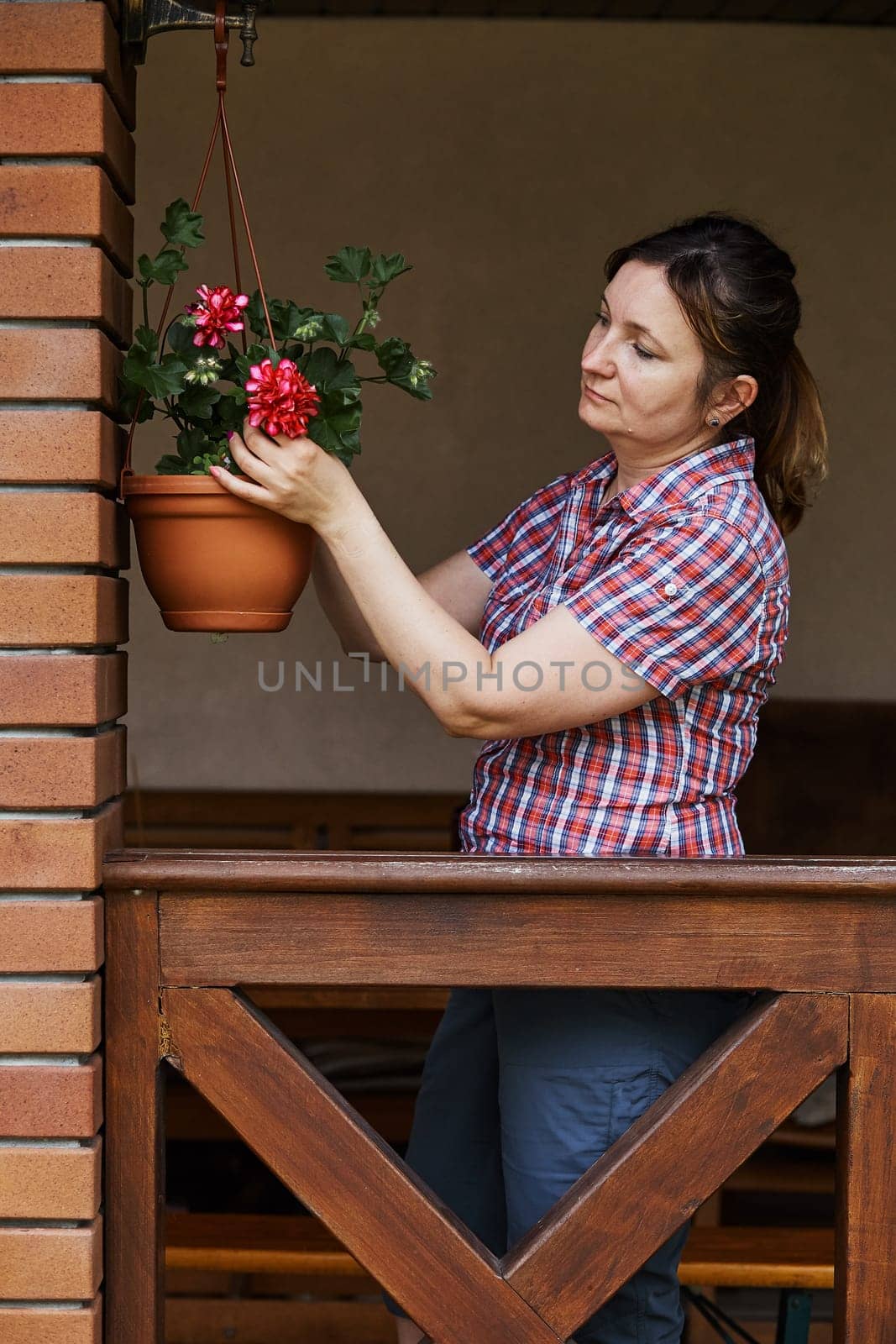 Woman arranging the flowers in a flower pot hanging on a patio. Candid people, real moments, authentic situations