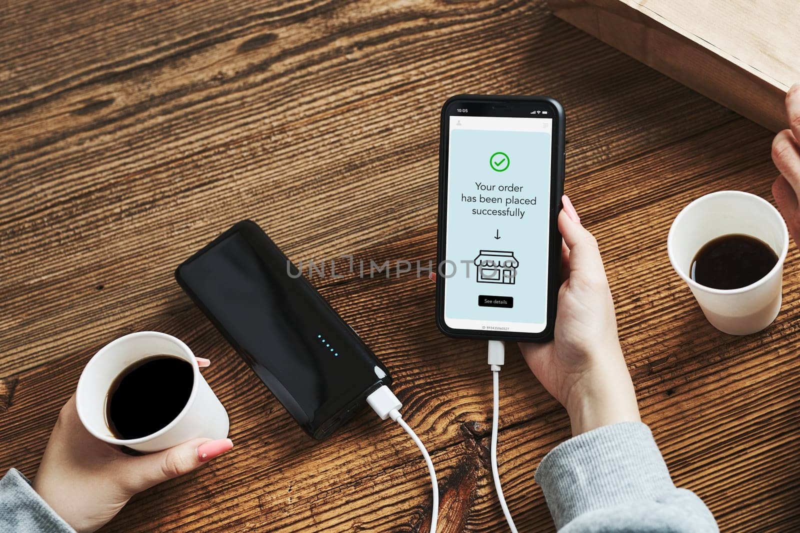 Online shopping. Buying online. Ordering product in online shop using smartphone. Order confirmation on screen. Online banking. People paying online. Paying for online shopping while charging mobile phone from powerbank in coffee shop
