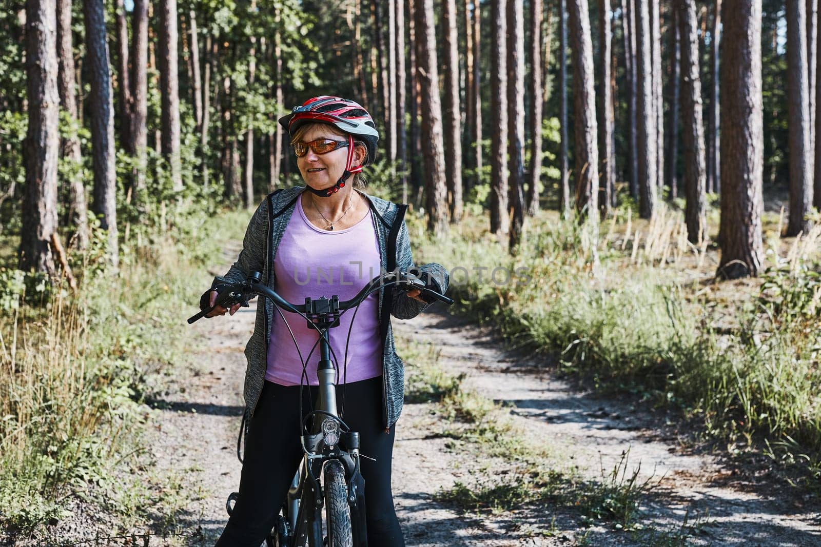 Active woman cycling on forest road. Female riding bicycle off-road route on summer vacation day. Woman wearing bicycle helmet and gloves