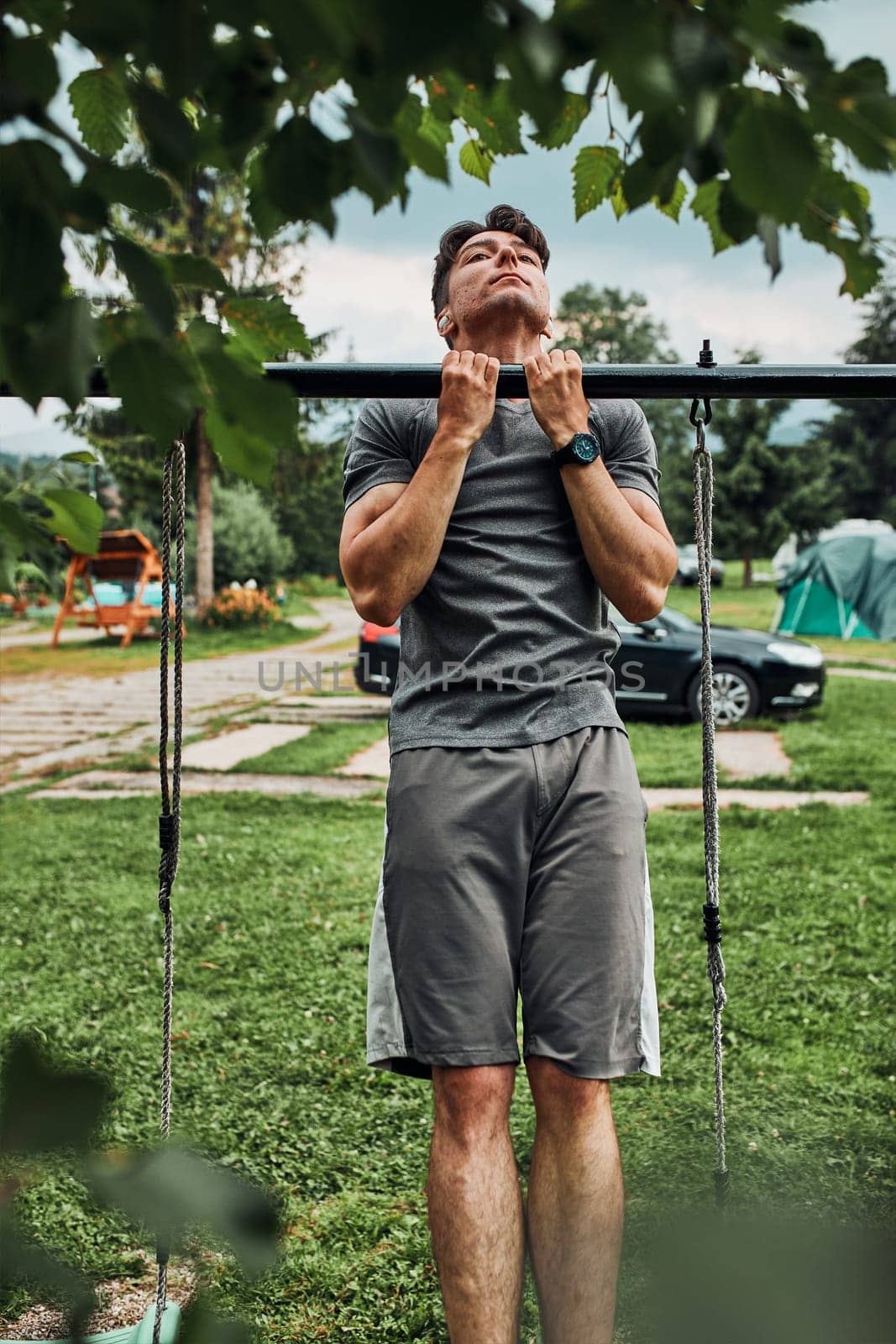 Young man doing pull-ups on pull-up horizontal bar during his calisthenics workout on a camping during his summer vacation trip