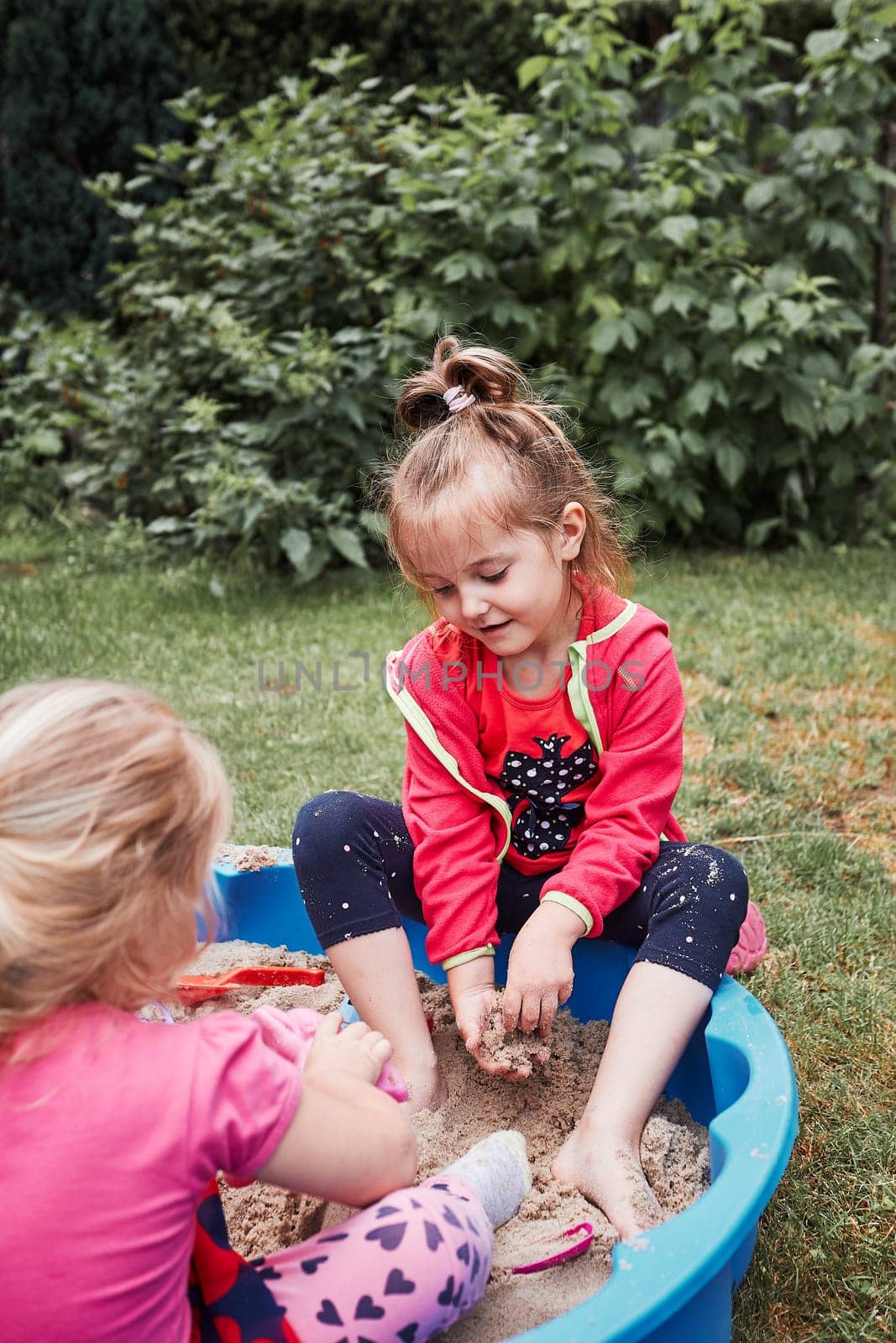Children, little girls, playing in sandbox in playground outside on summer day. Real people, authentic situations