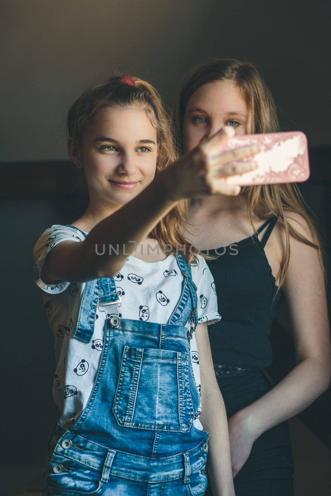 Young women taking selfie, using smartphone camera. Girls making faces, enjoying taking funny pictures together