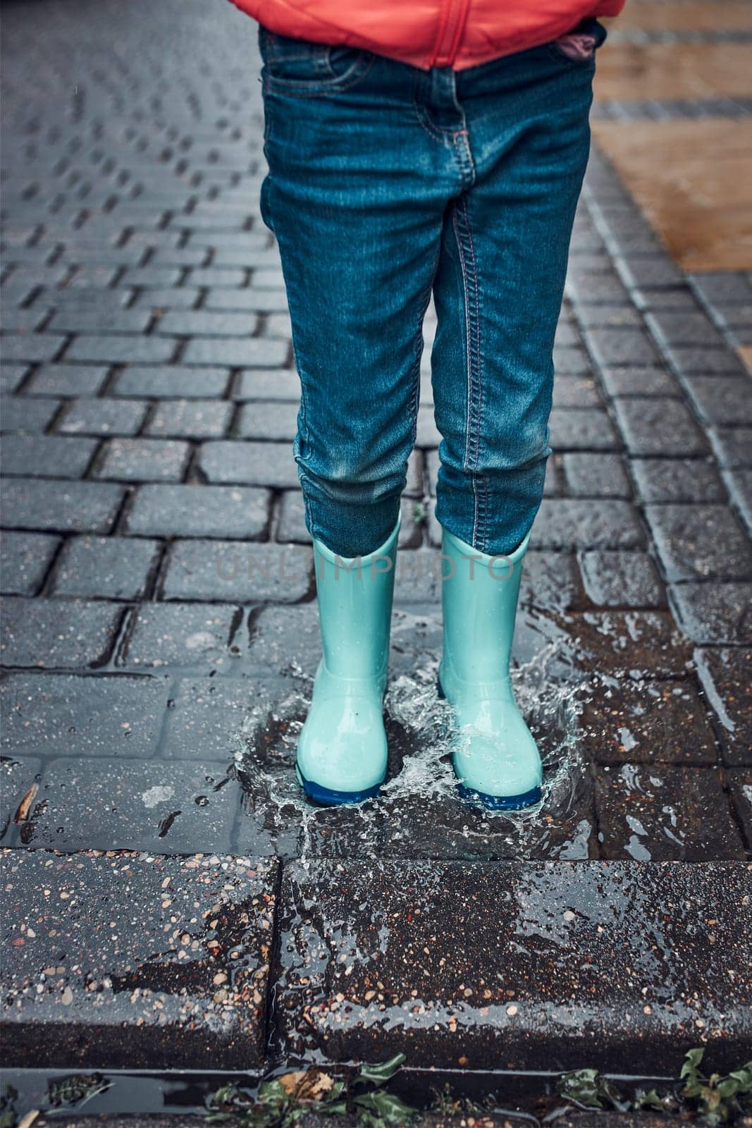 Close up of legs of little girl jumping in puddle wearing rubber boots walking in on rainy gloomy autumn day