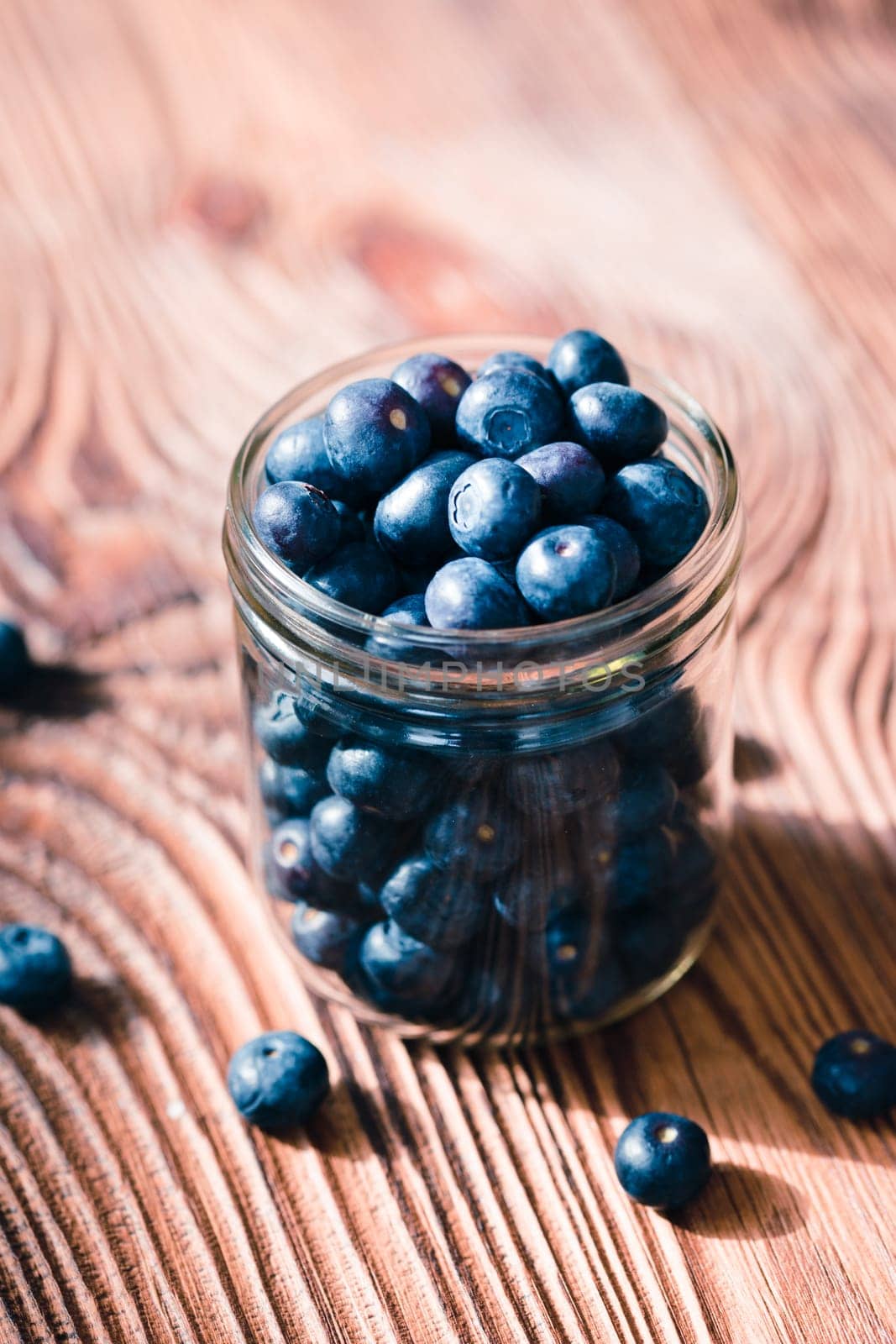 Freshly gathered blueberries put into jar. Some fruits freely scattered on old wooden table
