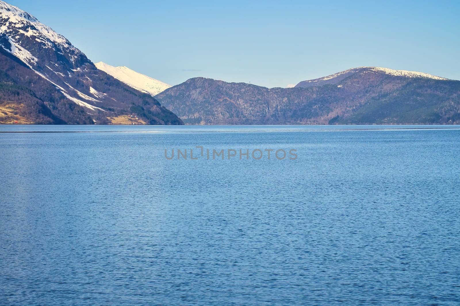 Fjord with snow covered mountains on the horizon. The water glistens in Norway. Landscape photo from the north