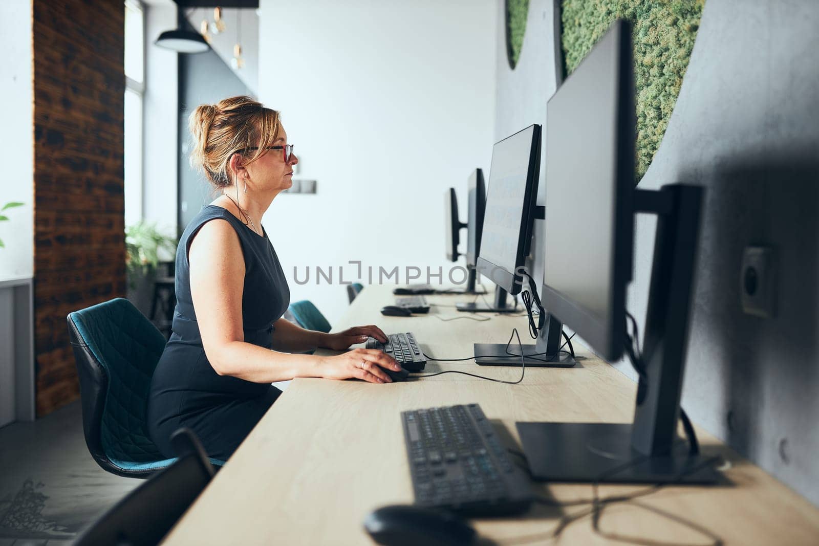 Concerned businesswoman working on computer in office. Busy woman sitting at desk at front of computer monitor. Focusing on work. Open office. Copy space right