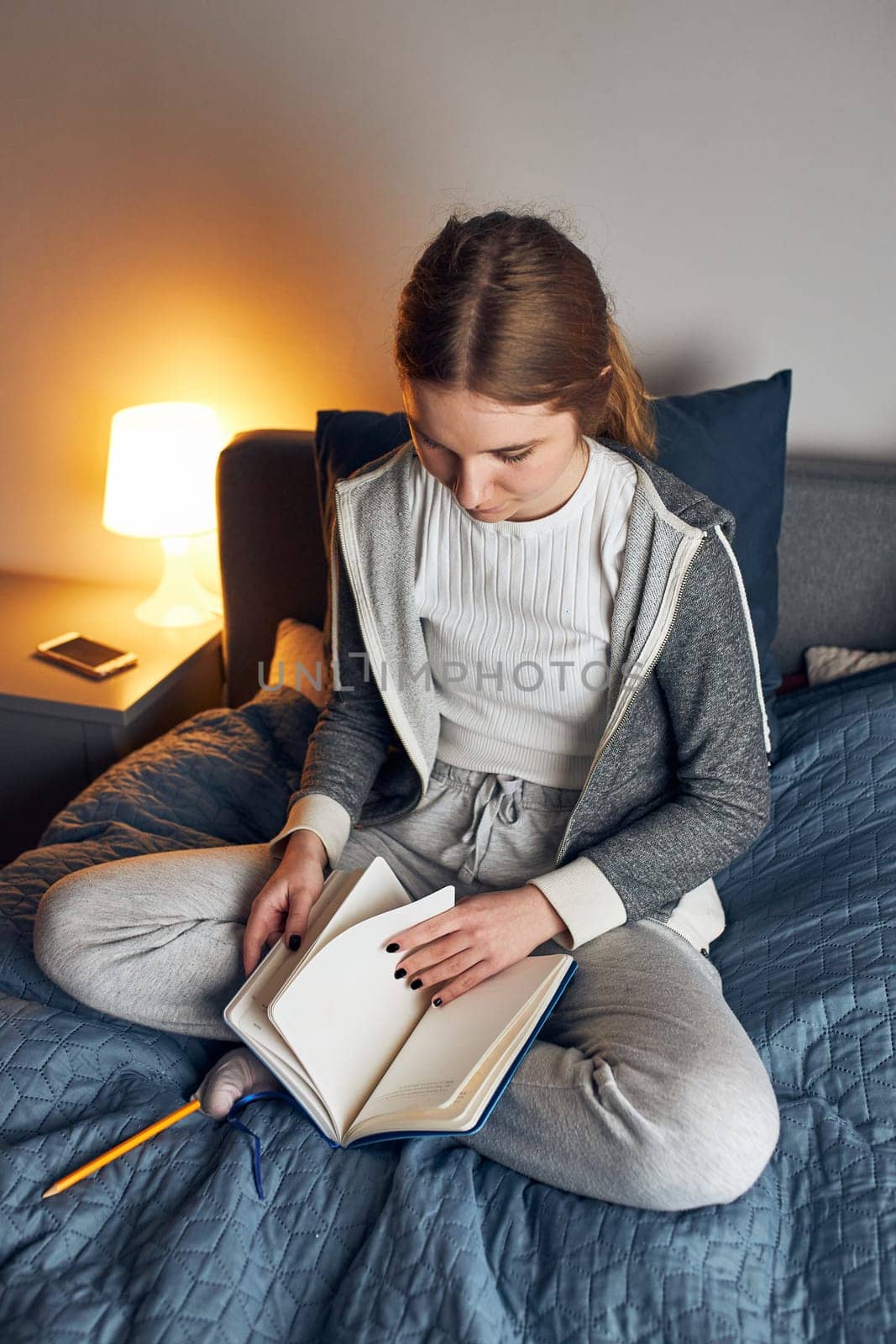Student learning at home. Young woman making notes, reading and learning from notepad sitting in bed at home during quarantine