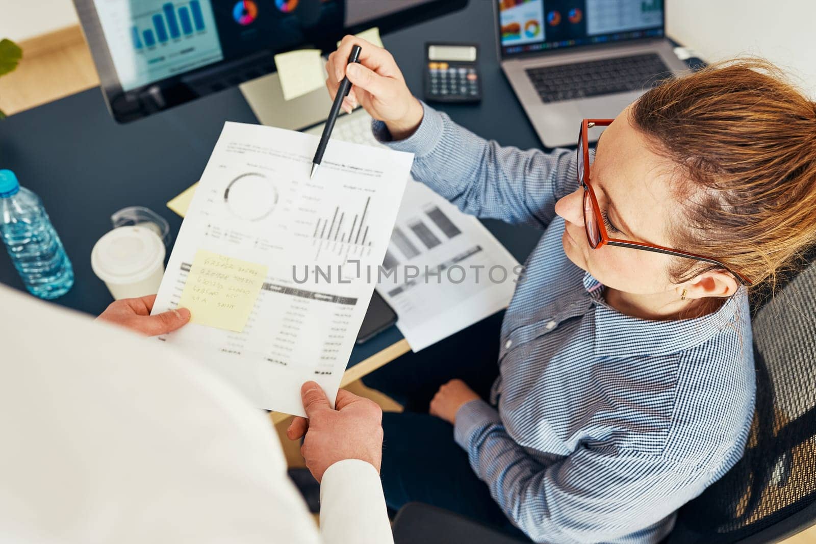 Businesswoman discussing financial data with her colleague sitting at desk in office. Woman entrepreneur working with charts and tables on computer. Two people working together. Workmates talking about project