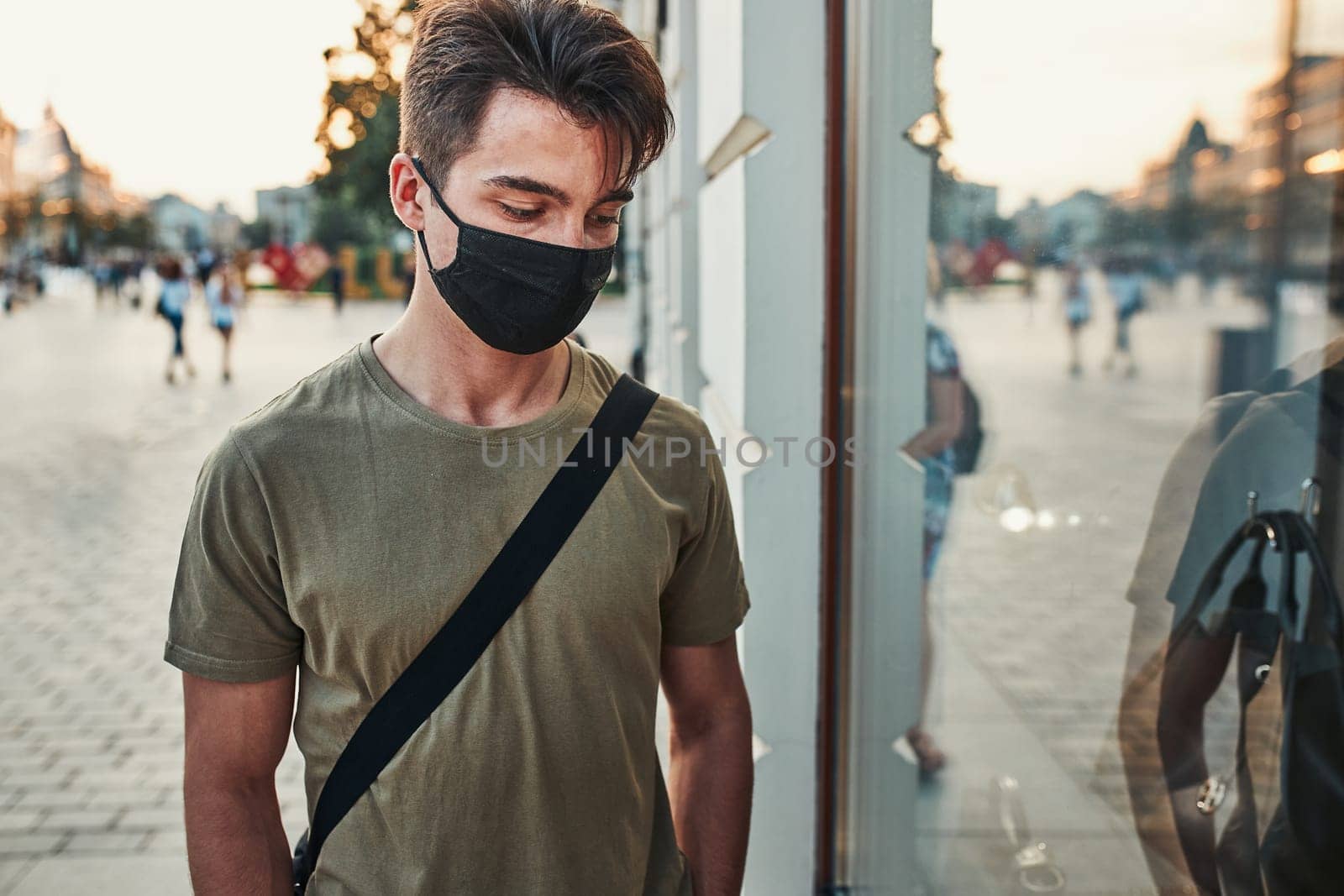 Young man walking along a store front in the city center in the evening wearing the face mask to avoid virus infection and to prevent the spread of disease in time of coronavirus
