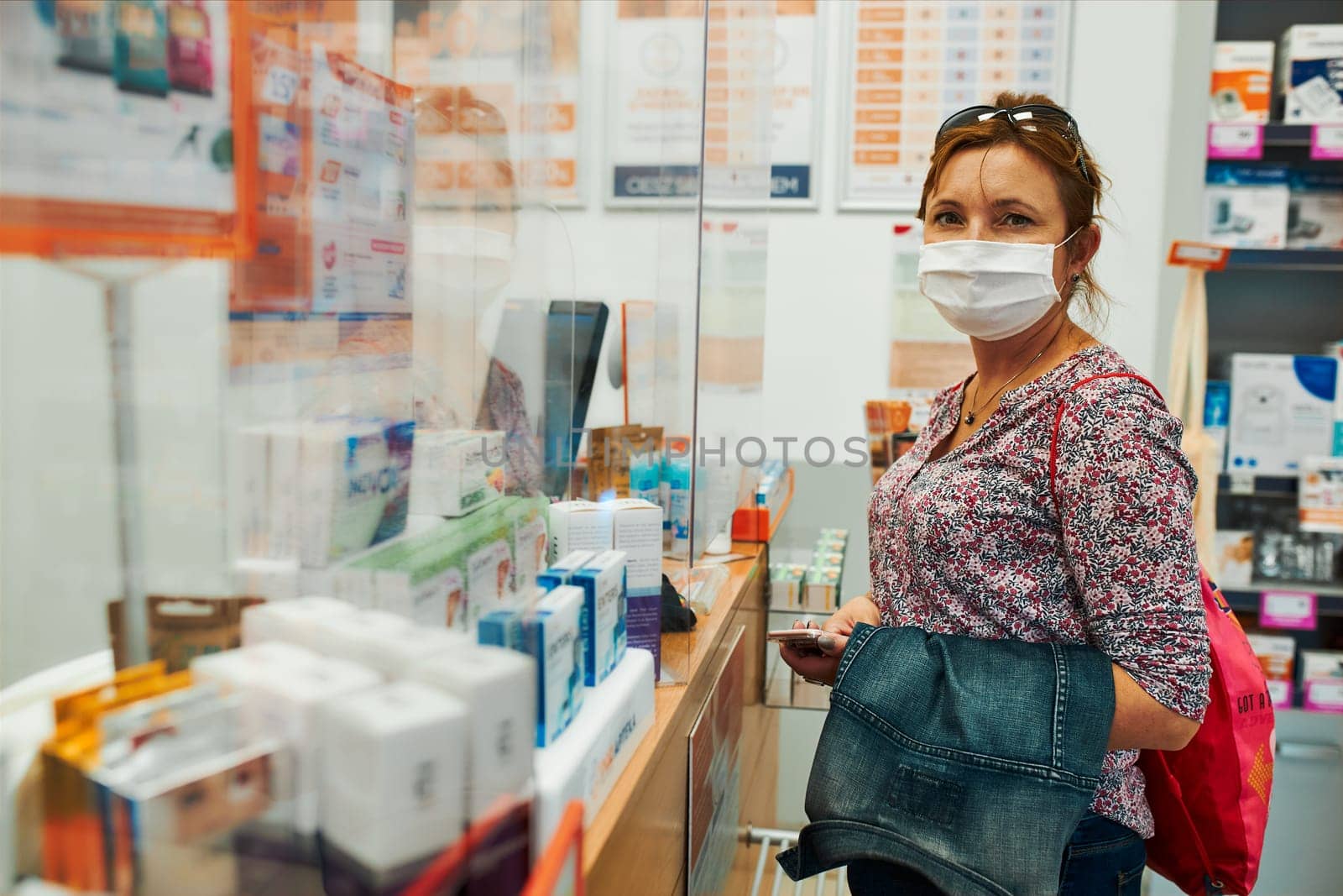 Woman shopping at pharmacy, buying medicines, wearing face mask to cover mouth and nose during pandemic coronavirus outbreak