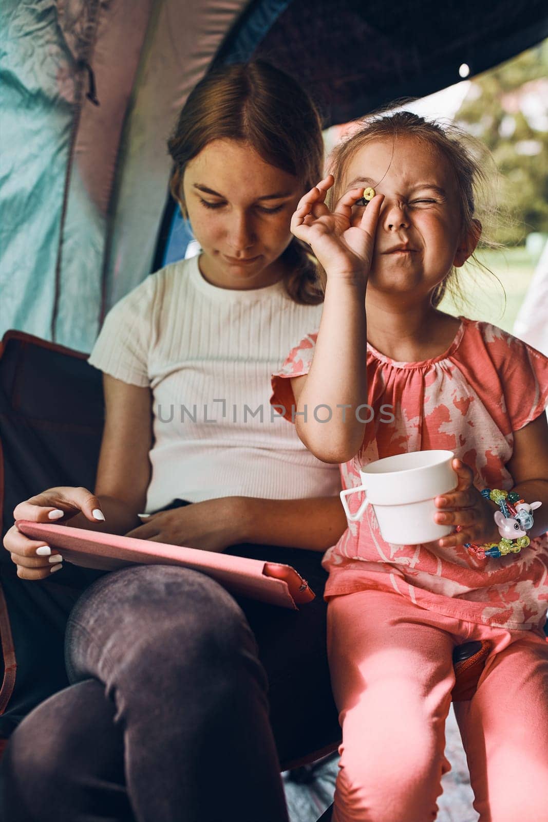 Two girls sisters spending family time in a tent on camping. Children using tablet playing games online during summer vacation