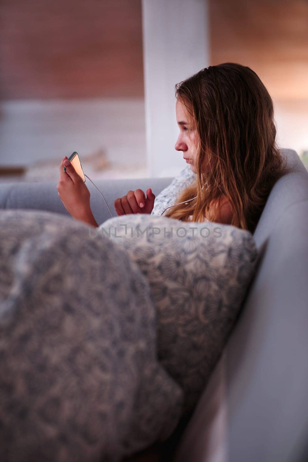Teenage girl watching video online on smartphone sitting on sofa at home