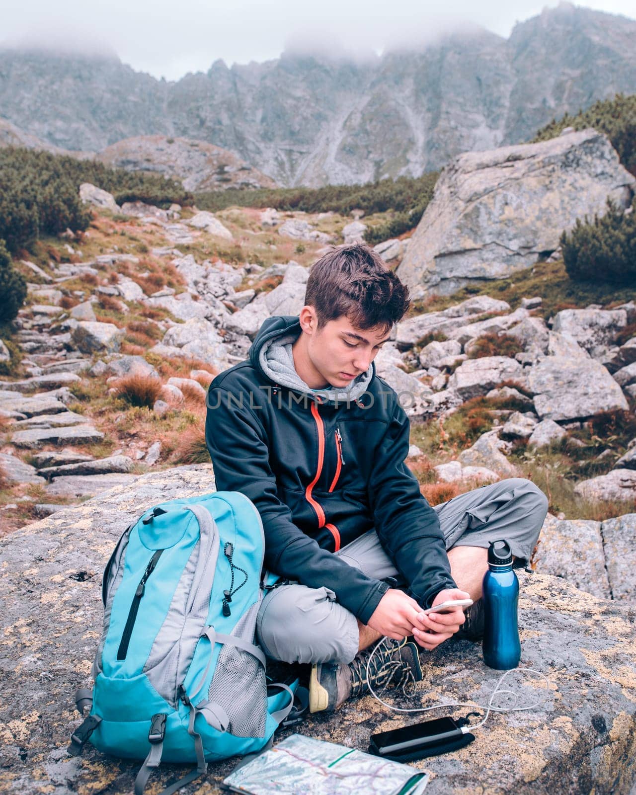 Boy resting on a rock and charging a mobile phone during trip in the Tatra Mountains