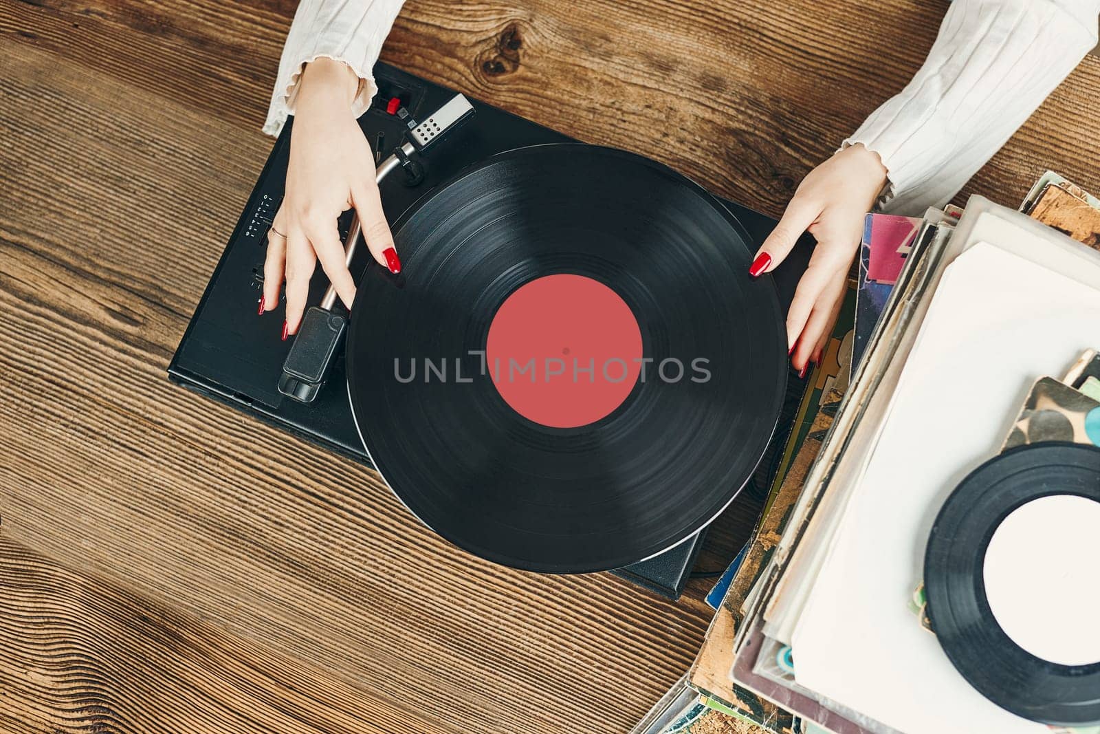 Young woman listening to music from vinyl record player. Playing music on turntable player. Female enjoying music from old record collection at home. Stack of analog vinyl records. Retro and vintage music style. Music Passion and hobby