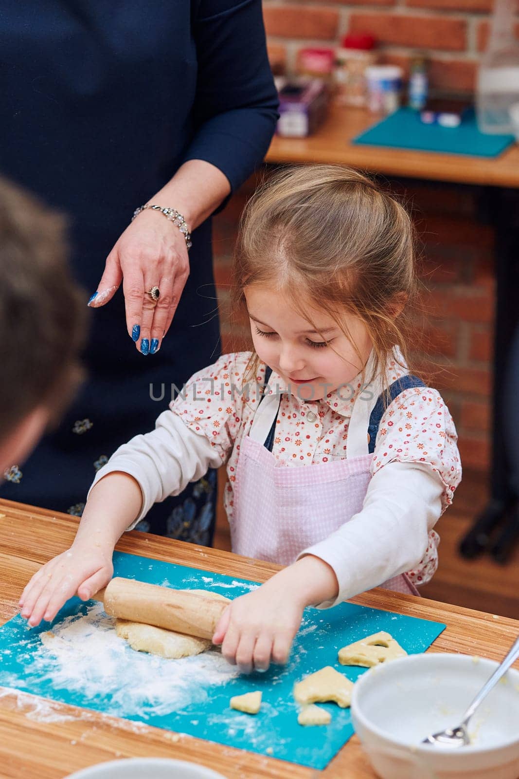 Little girl rolling the dough with her mom's help for the cookies. Cutting the dough to heart shapes. Kid taking part in baking workshop. Baking classes for children, aspiring little chefs. Learning to cook. Combining and stirring prepared ingredients. Real people, authentic situations