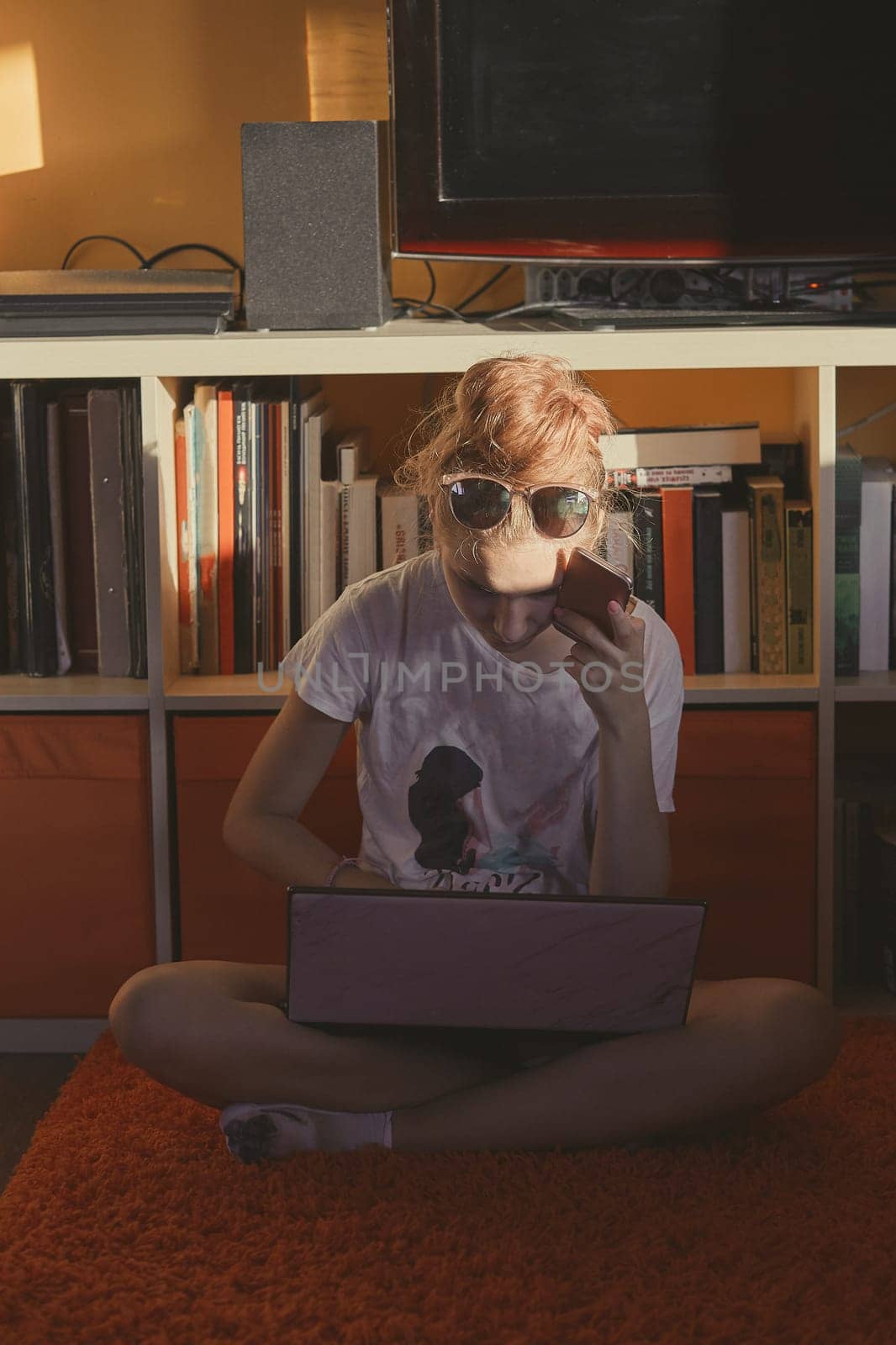 Young woman using portable computer and mobile phone, sitting on a floor, learning online at home. Candid people, real moments, authentic situations