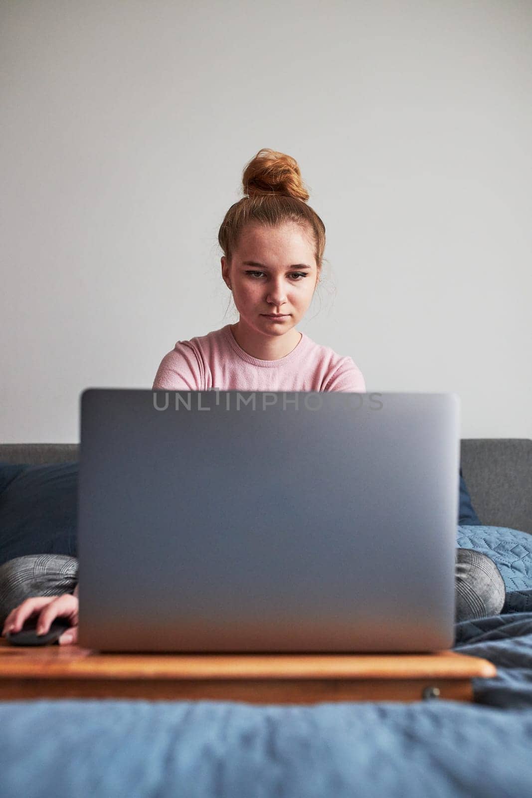 Teenage girl working on school tasks homework remotely on her laptop from home during COVID-19 quarantine. Online course lessons. Learning remotely. Girl sitting on bed in front of computer looking at screen