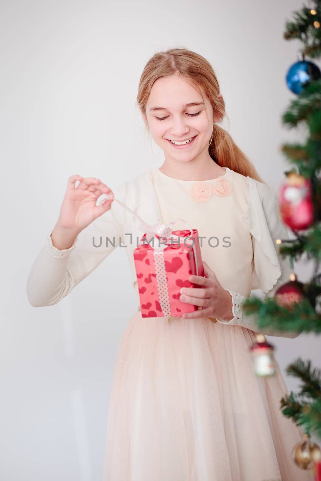 Happy girl unpacking Christmas gift standing behind a tree