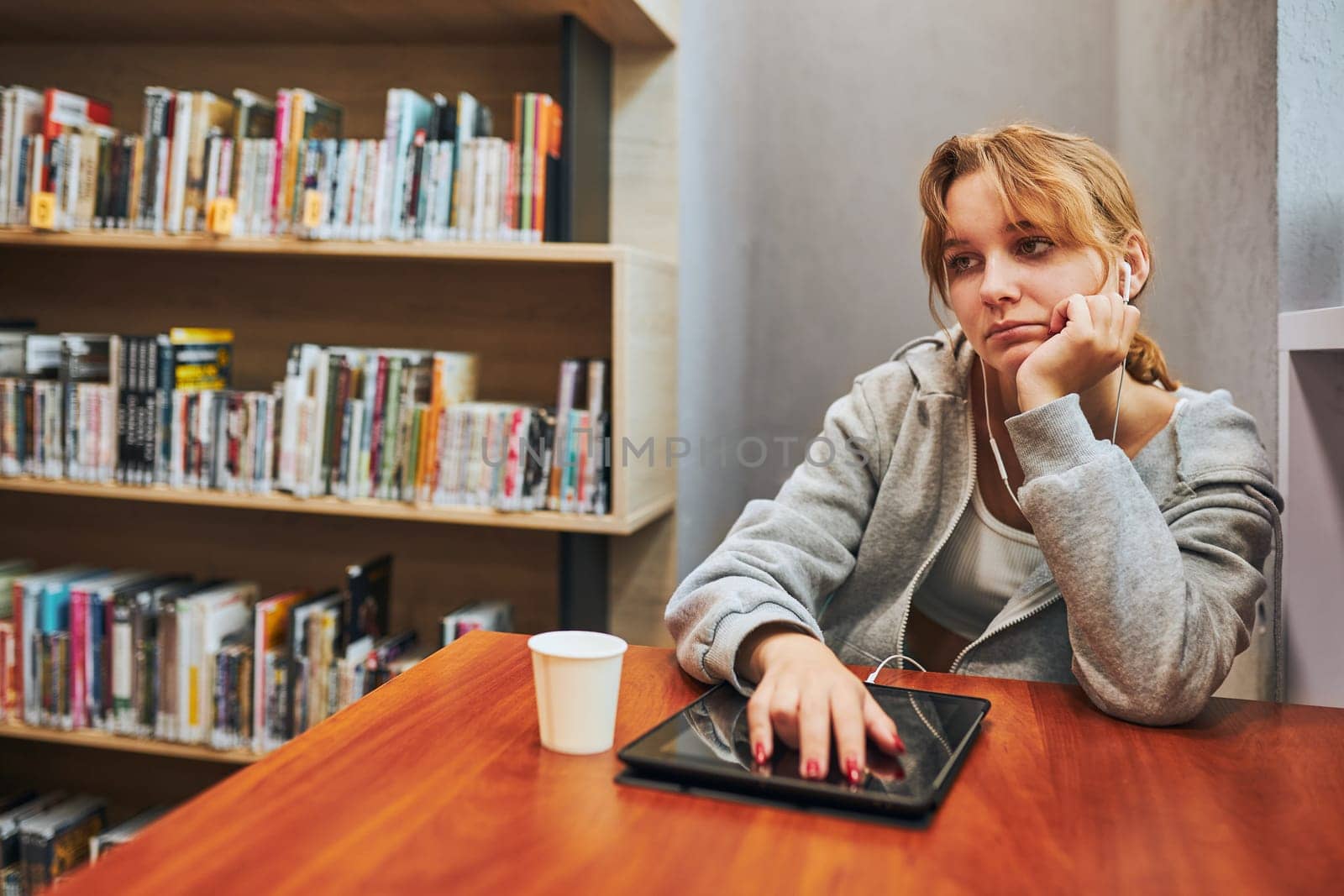 Bored student learning in university library. Young woman listening to online course from computer. Remote education. Using technology. Back to school