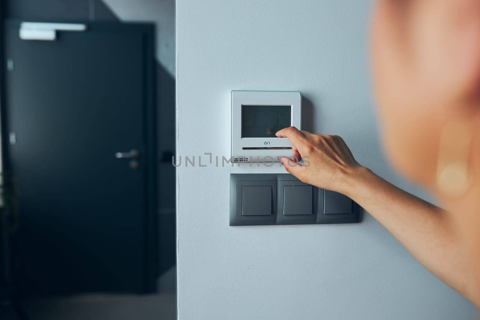Woman controlling office with digital touch screen panel installed on the wall in office. Concept of smart remote control. Managing system at work. Woman using digital device to activate lock system at smart office