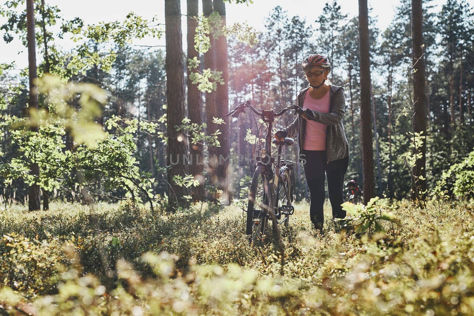 Active woman cycling on forest road. Female riding bicycle off-road route on summer vacation day. Woman wearing bicycle helmet and gloves