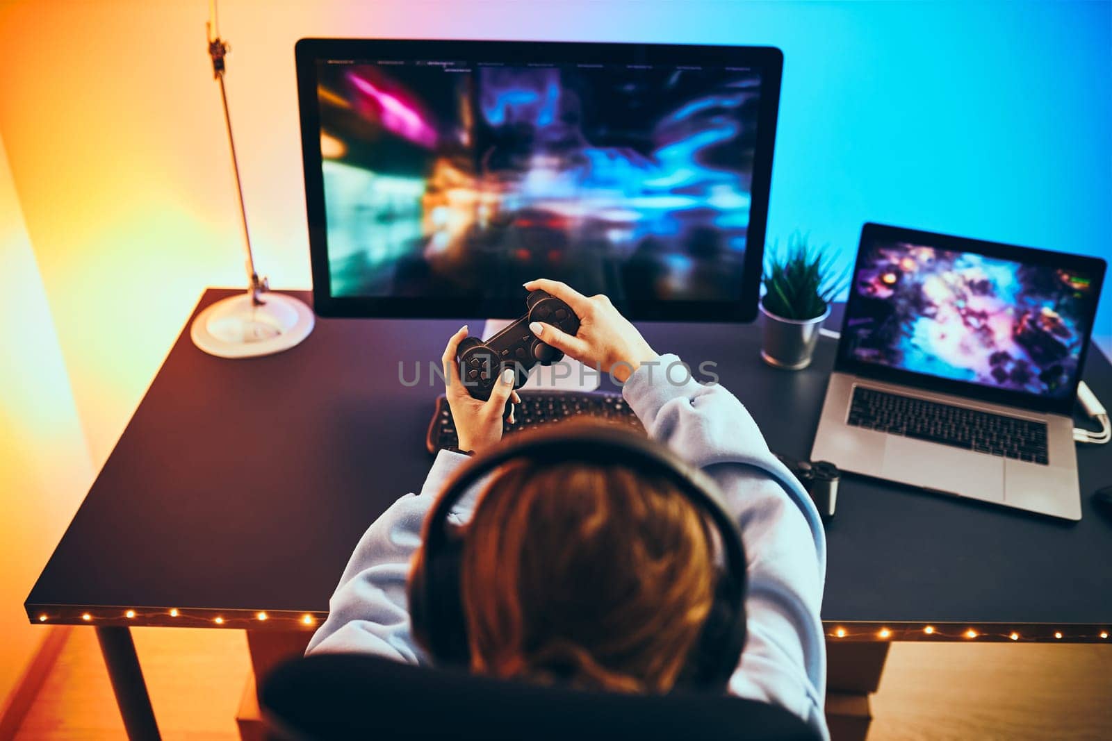 Teenager girl playing video game at home. Gamer holding gamepads sitting at front of screen. Streamer playing online in dark room lit by neon lights. Competition and having fun