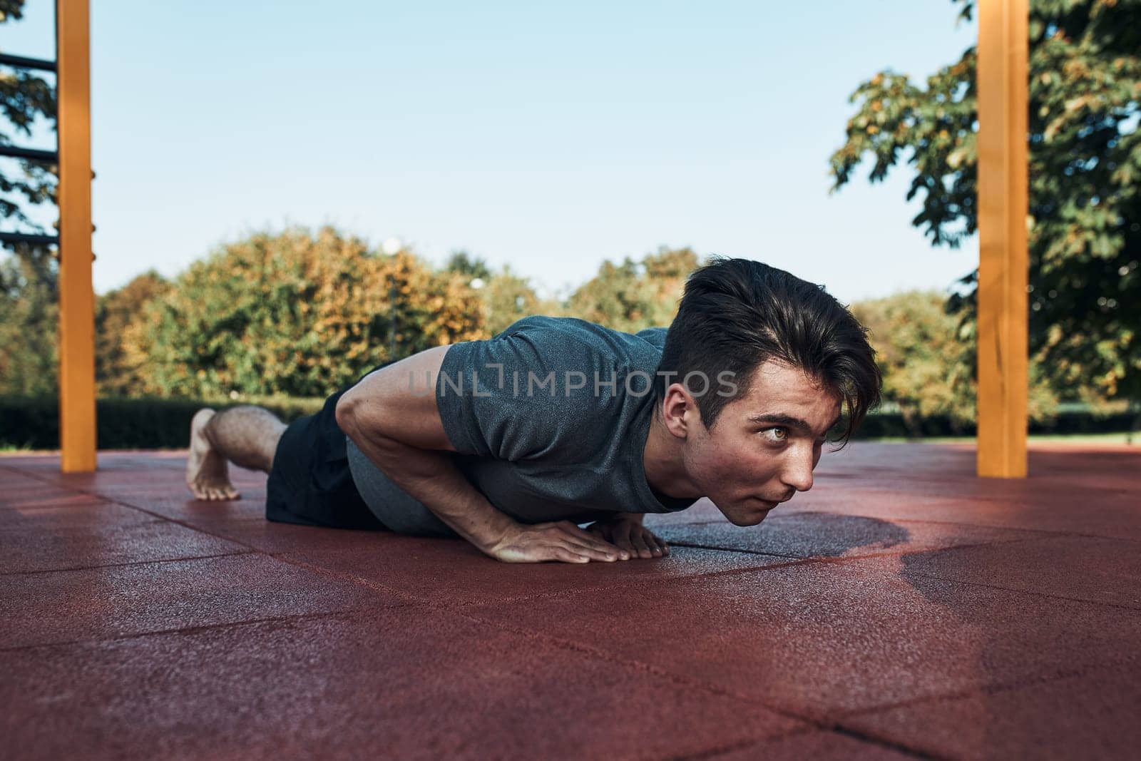Young man doing push-ups on a red rubber ground during his workout in a modern calisthenics street workout park. Man wearing sportswear looking away