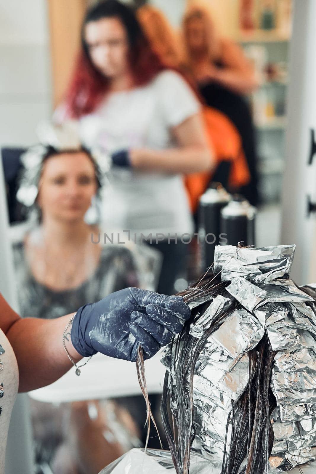 Hairdresser styling dyeing combing womans hair. Young woman working as a hairdresser in hair salon. Real people, authentic situations