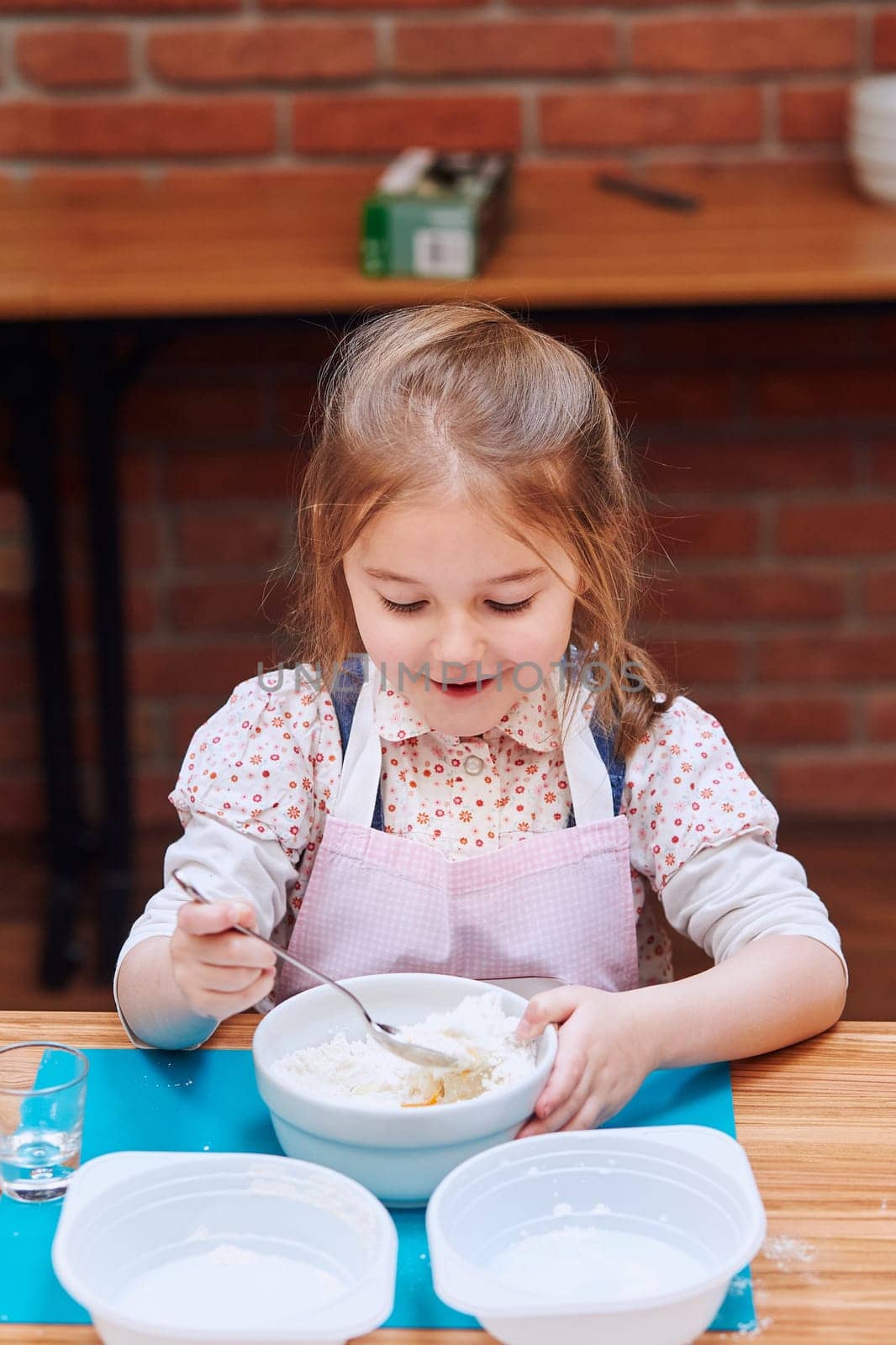 Little girl combining the ingredients for baking the cake. Kid taking part in baking workshop. Baking classes for children, aspiring little chefs. Learning to cook. Combining and stirring prepared ingredients. Real people, authentic situations