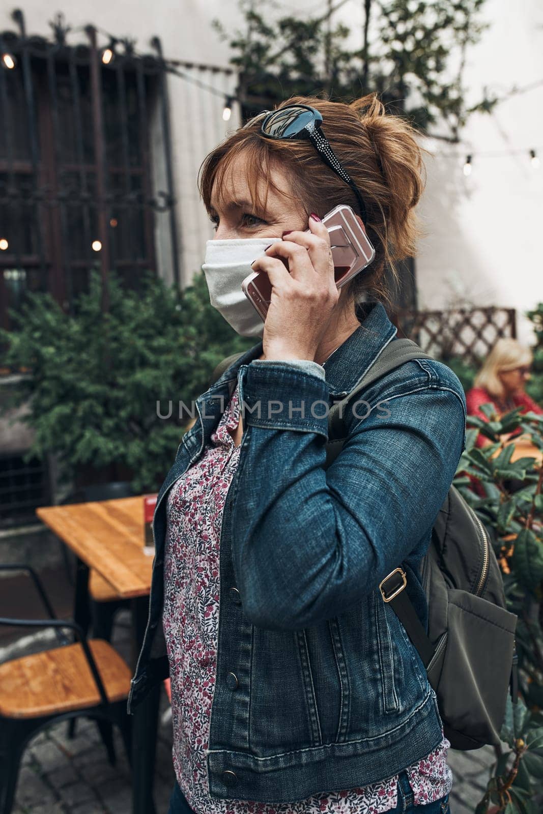 Young woman talking on phone standing in a street downtown. Woman is wearing the face mask to avoid virus infection and to prevent the spread of disease in time of coronavirus