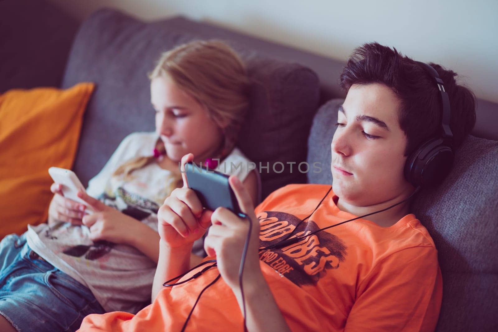 Girl and boy using smart phones, listening to music, playing the games sitting on a couch at home