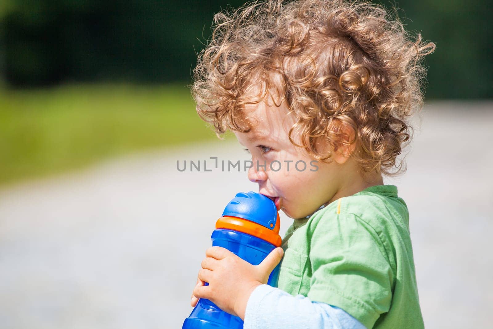 The portrait of a 1 and a half year old baby boy drinking water outdooors.