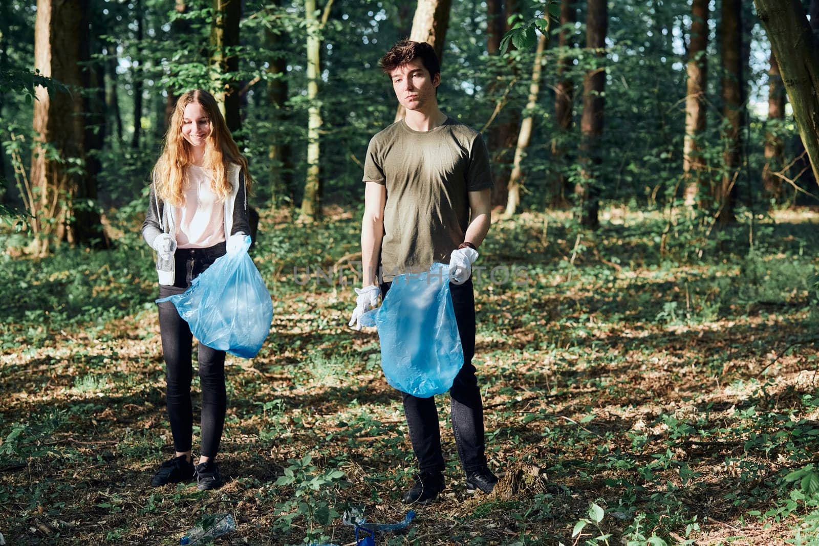 Young man and woman cleaning up a forest. Volunteers picking plastic waste to bags. Concept of plastic pollution and too many plastic waste. Environmental issue. Environmental damage. Responsibility for environment. Real people, authentic situations